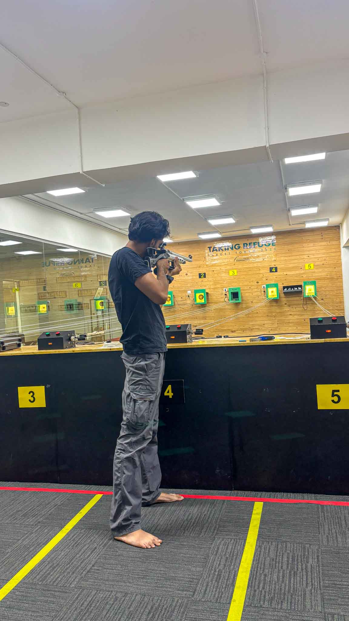 Man shooting a rifle barefoot at an indoor shooting range with numbered target boards in Bengaluru's best shooting experience.